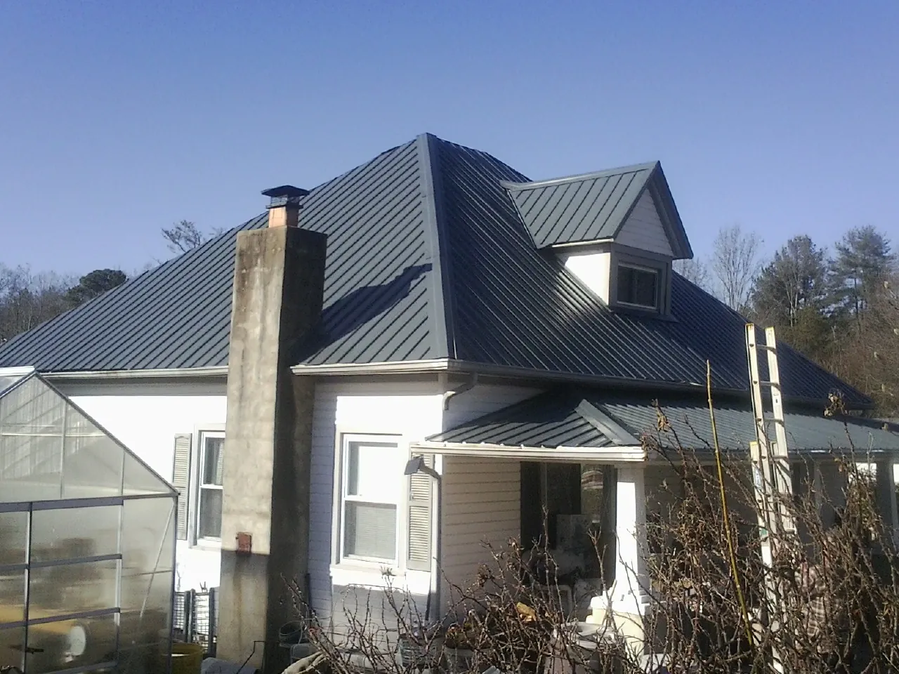 Dark blue standing seam metal roof on a white farmhouse with dormer — Slate & Tile Roof Repair by Roofing Brothers in Pacific Junction
