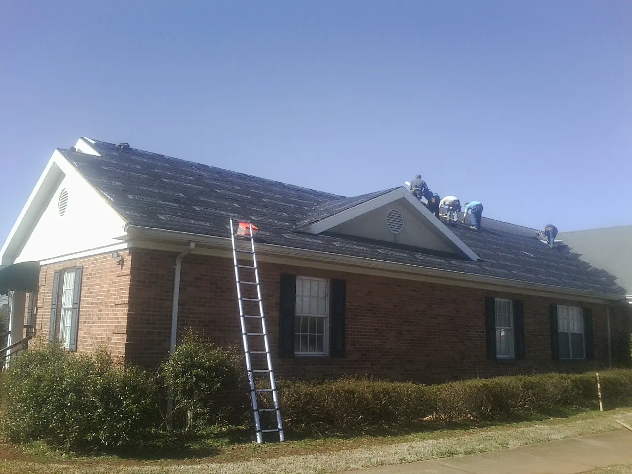 Crew tearing shingles off a brick ranch roof with a ladder set — Metal Roof Repair work by our crew in Pacific Junction