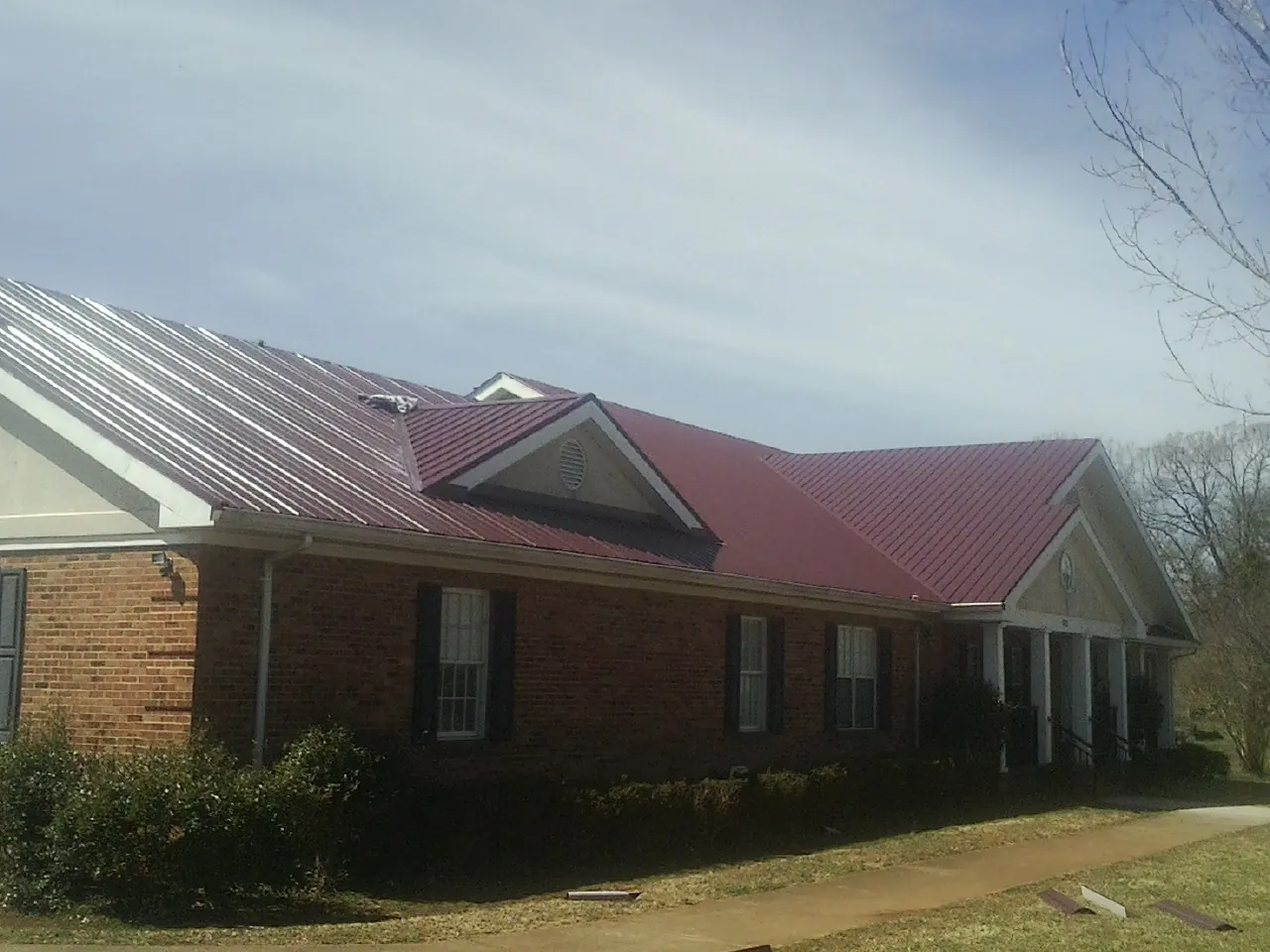 Red metal roof with gabled entries on a long brick building, from a Hail Damage Roof Repair job in Pacific Junction