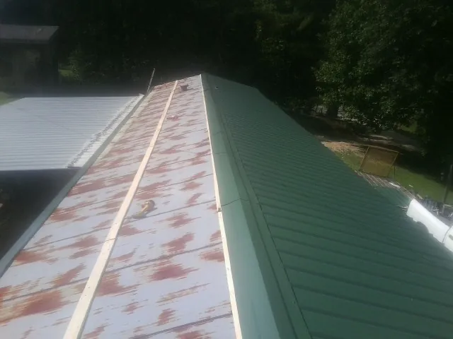 Old rusted panels beside newly installed green metal roofing — Wind Damage Roof Repair by Roofing Brothers in Pacific Junction
