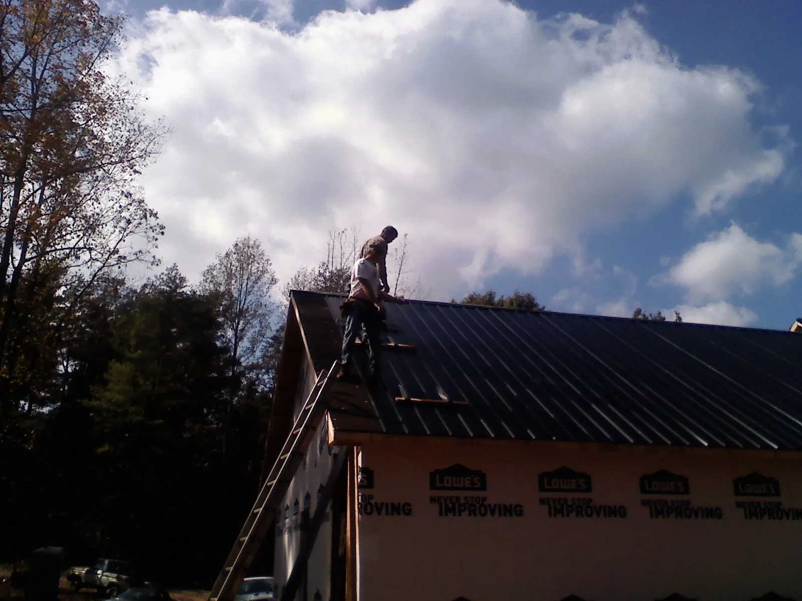 Roofer fastening dark metal panels high against a cloudy sky, from a Roof Inspection job in Pacific Junction