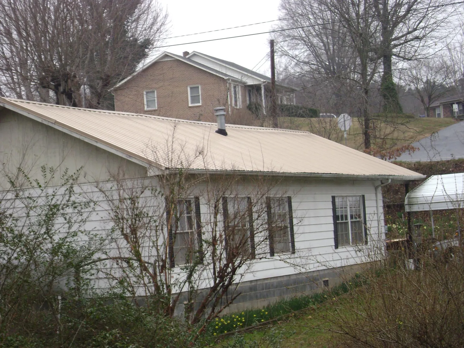 Tan metal roof on a white sided house set into a hillside — Commercial Roofing by Roofing Brothers in Pacific Junction