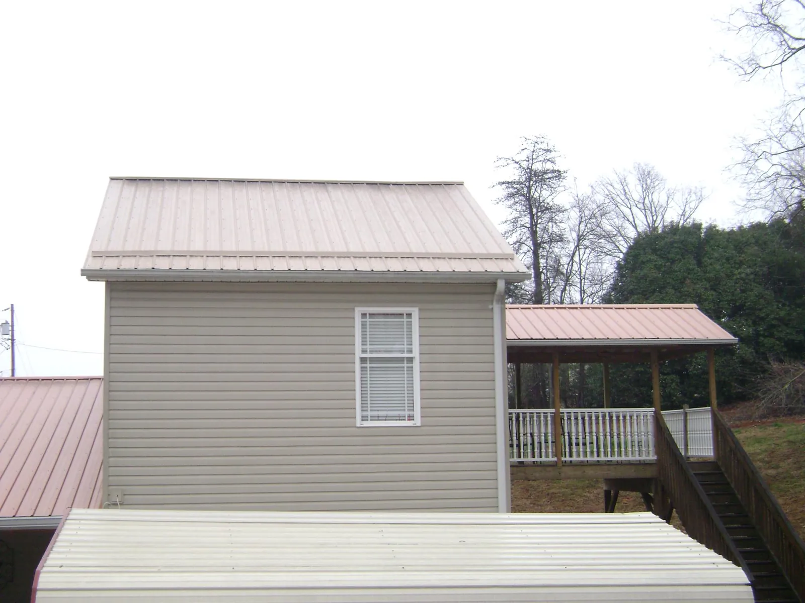 Tan metal roofs on a two story addition and attached porch, from a Roof Replacement job in Pacific Junction